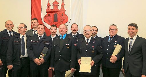 Kommandant Jürgen Rauer (links) und Bürgermeister Bruno Metz (rechts) gratulieren mehreren Feuerwehrleuten zum Dienstjubiläum.   Foto: Decoux-Kone